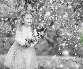 Stunning black and white portrait little girl laughs and has fun in a flying skirt and a fur blouse with a bouquet of blossoming cherry flowers in a spring garden. Daughter's day. Easter