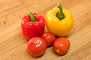 Red and yellow bell pepper with tomato on wooden chopping board.