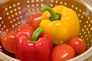 Red and yellow bell pepper with tomato in punched metal basket.