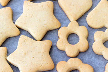 Baked shortbread cookies in the form of stars, hearts and flowers on a baking sheet with parchment paper just taken out of the oven. Tea snack for breakfast. Selective focus. Closeup view