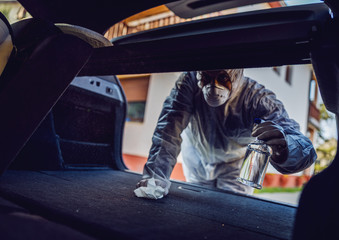 Man in protective suit with mask disinfecting inside car, wipe clean surfaces that are frequently...