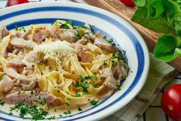 Italian fettuccine pasta in cheese sauce with parmesan, chicken and ham, herbs in white ceramic bowl on white background.