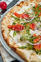 Tasty pizza with cheese, cherry tomatoes, salmon, arugula and parmesan on a wooden background. Italian traditional cuisine. Top view. Food for lunch. Half of pizza