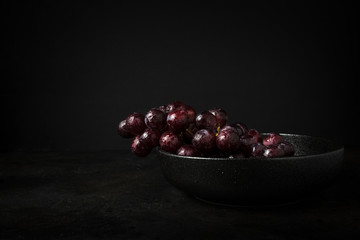 Still life of a bunch of very fresh red grapes in a black bowl. Photography Vintage and dark style