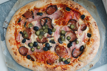 round hot pizza with hum, sausage,cucumber, olives onion and cheese close up photo