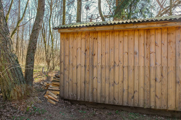 Chopped firewood near a wooden house on a sunny day in Ukraine. Firewood stacked on the ground. Little house in the forest.