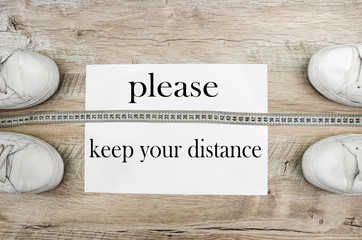 the inscription "please keep your distance." White sneakers and measuring tape on a wooden background. The concept of quarantine during a pandemic.