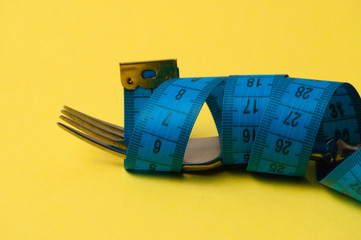 Centimeter and fork on a yellow background. Concept diet, healthy nutrition and weight loss
