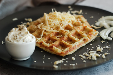Tasty waffles with zucchini and cheese. Waffles served with cheese, onions, sour cream and spices. Waffles on a plate