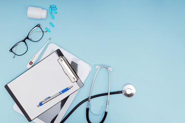 Workplace of modern doctor concept. Tablet, glasses, pills, stethoscope and other objects on blue background