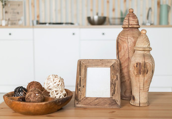 Fototapeta na wymiar a wooden table with wooden vases and a photo frame, a vase with decorative wicker balls on the background of a white kitchen set with dishes in the interior