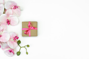 flatlay of single Gift present box with pink ribbon with orchid flowers on white background. spring concept. Copy space