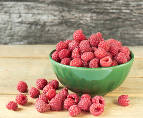 Raspberry in a bowl with  berries scattered around on wooden table on rustic background, closeup, copy space, healthy vegan eating and organic homegrown food concept