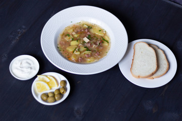 Solyanka soup with fermented cabbage, meat, lemon, olives, sour cream, bread on black wooden background