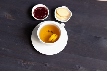 cup of herbal tea with floating lemon, ginger, cranberry jam on  black wooden background