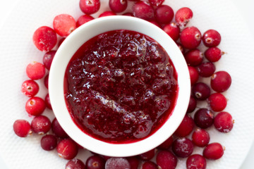 Crenberry jam in white bowl  and frozen fresh moos-berries on white plate