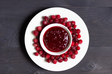 Crenberry jam in white bowl  and frozen fresh moos-berries on black wooden background