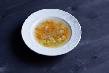 White plate with cabbage vegetarian soup on black wooden background