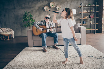 Photo of grandpa sit sofa play guitar little pretty granddaughter hold mic singing song spend time...