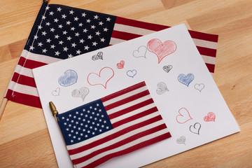 Multiple red blue and gray hearts are hand-drawn on a white sheet of paper with two American flags 