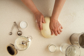 Obraz na płótnie Canvas Female hands kneading dough on tabletop. Various kitchen utensils, ingredients. Home baking concept