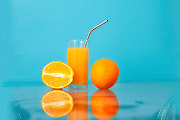 Fruit oranges and orange juice at the glass transparent kitchen table on the light colorful blue background Fresh summer