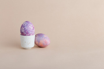 Minimal easter two eggs. Purple and pink colored eggs in cup at pastel beige background