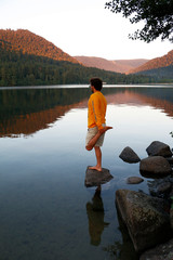 Male model performing various yoga poses/asanas on a rock in a lake