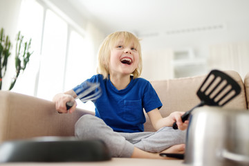 Mischievous preschooler boy play the music using kitchen tools and utensils at home during...