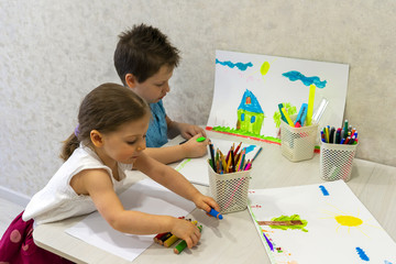 A boy and a girl draw at the table with pencils and markers