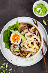 Traditional asian noodle soup pho in bowl, garnished with egg, mushrooms on concrete background. Asian food concept.