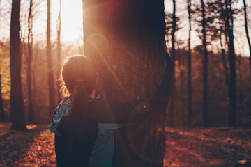 Beautiful scene of a sporty woman hugging a tree in forest at sunset. 