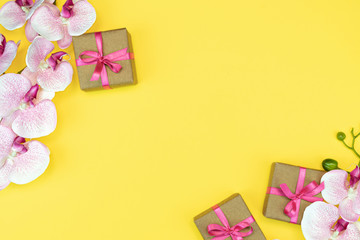 flat lay of Gift present boxes with pink ribbon on yellow background with orchid flower. spring concept. Copy space