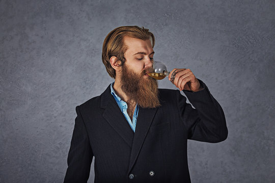 Handsome bearded well-dressed man in jacket holding glass of beverage whiskey
