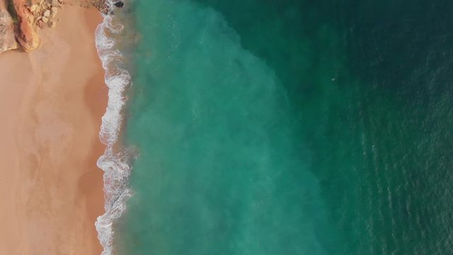 Top down aerial waves crashing pristine beach Praia dos Caneiros Portugal emerald ocean
