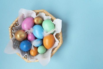 Fototapeta na wymiar Golden, pink, blue, green, orange eggs in the wicker basket on the blue background. Copy space. Place for text and design. Happy Easter. Top view. Flat layout.