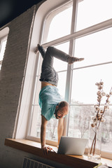 Fototapeta premium Inspired. Young man doing yoga at home while being quarantine and freelance online working. Remote office, isolated. Concept of healthy lifestyle, wellness, being safe while coronavirus pandemic.