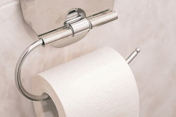 Closeup of a toilet roll holder in a bathroom. One roll of toilet paper on a silver holder.