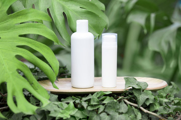 White clear tube for skincare bottle on bamboo plate over tropical leaves background. Skincare spray tube for helthcare concept.