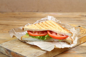 Sandwich with tomatoes, cheese and ham on a dark, wooden background