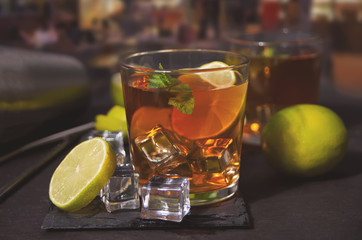 Fresh cocktail Cuba Libre with brown rum, cola, mint and lime on black background. Long Island Iced Tea cocktail.