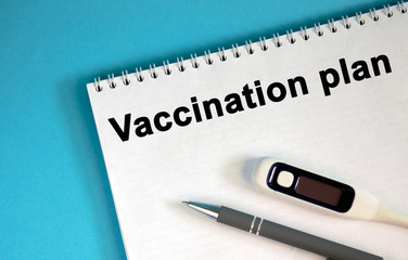 VACCINATION PLAN - text on a notepad. Lie a pen and a medical thermometer