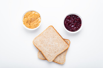 Bread slices, peanut butter and lingonberry jam on a white background, top view