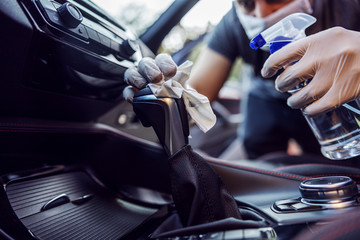 Man in protective suit with mask disinfecting inside car, wipe clean surfaces that are frequently...