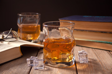 whiskey with ice on a wooden table. Nearby old books.