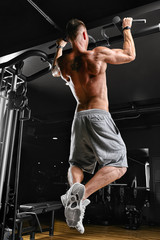 The athlete does pull-ups - chin in the gym, model with a sports body topless. Shot from the back, low key,