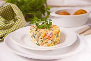 Russian traditional salad Olivier with vegetables and meat in the white plate.
