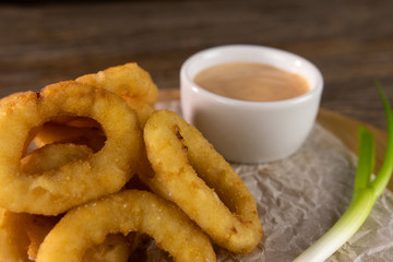 fried onion rings with sauce and green leek on paper close up