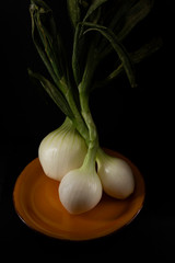 Three onions in a mustard colored bowl on black background
