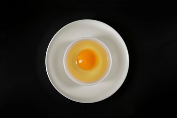 Aerial view of an egg: on a white plate another plate, inside, an egg white and an egg yolk, all on a black background